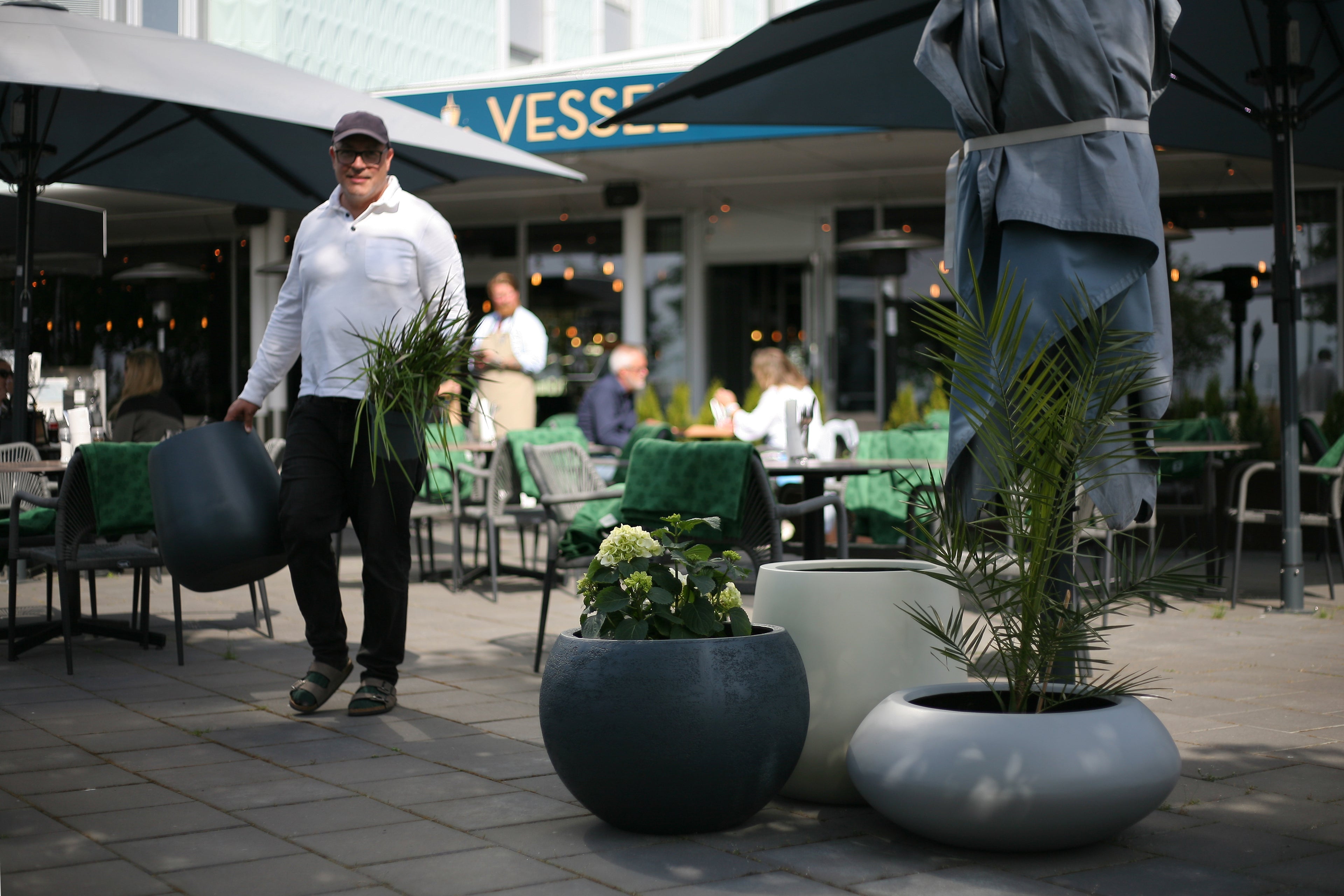 Man standing beside planters of outside a restaurant holding another pot and another plant.