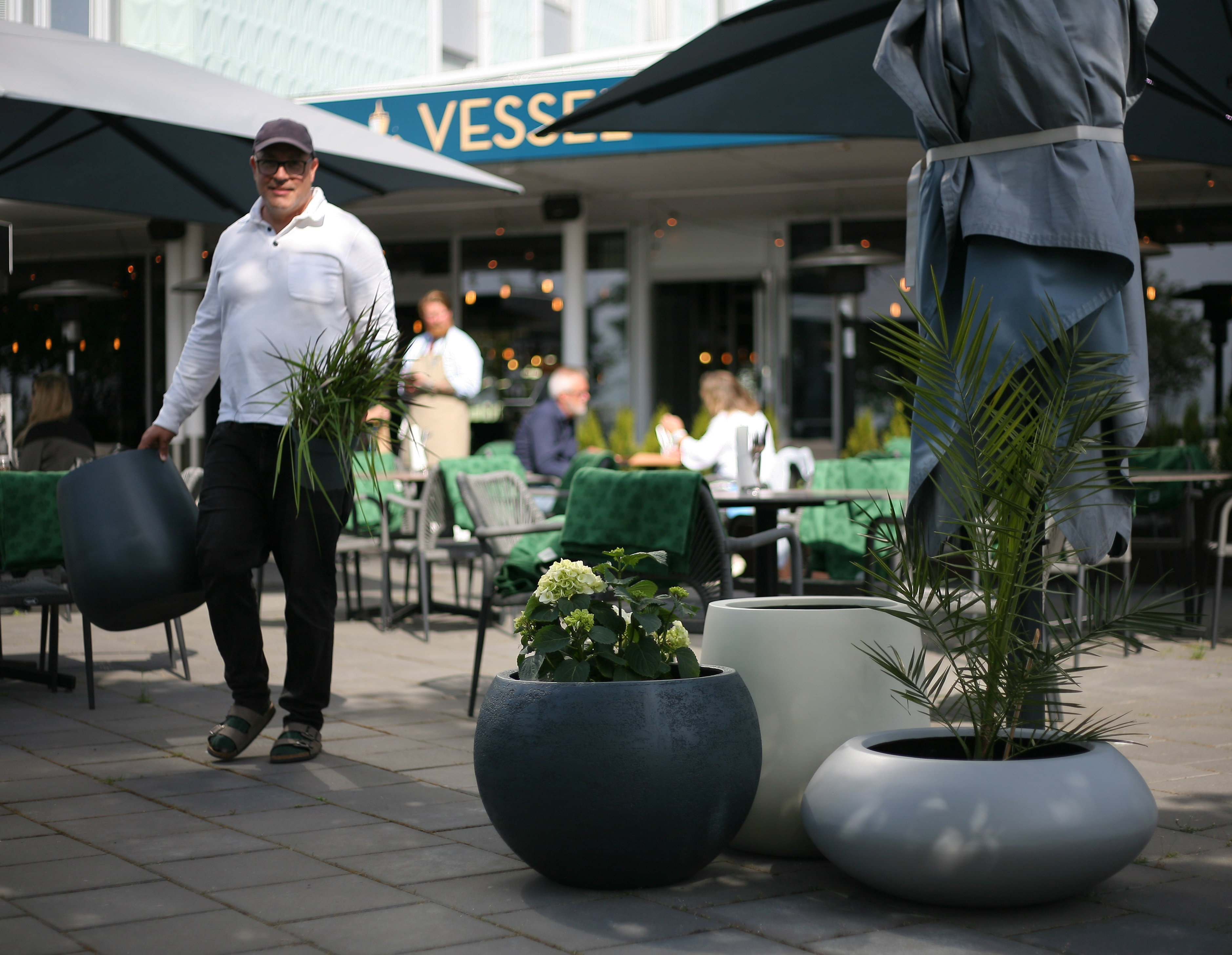 Man standing beside the planters at the outdoors of a cafe,
